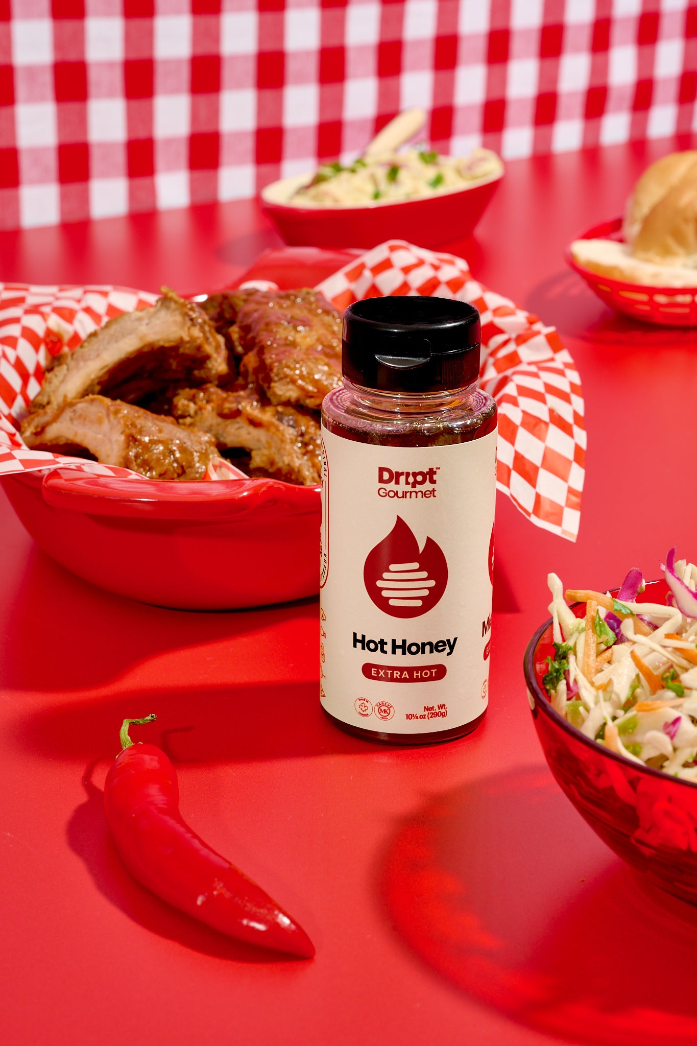 Dript Gourmet extra hot honey ribs on a red tray with coleslaw, hot pepper and a bottle of Extra Hot Honey on a red table.