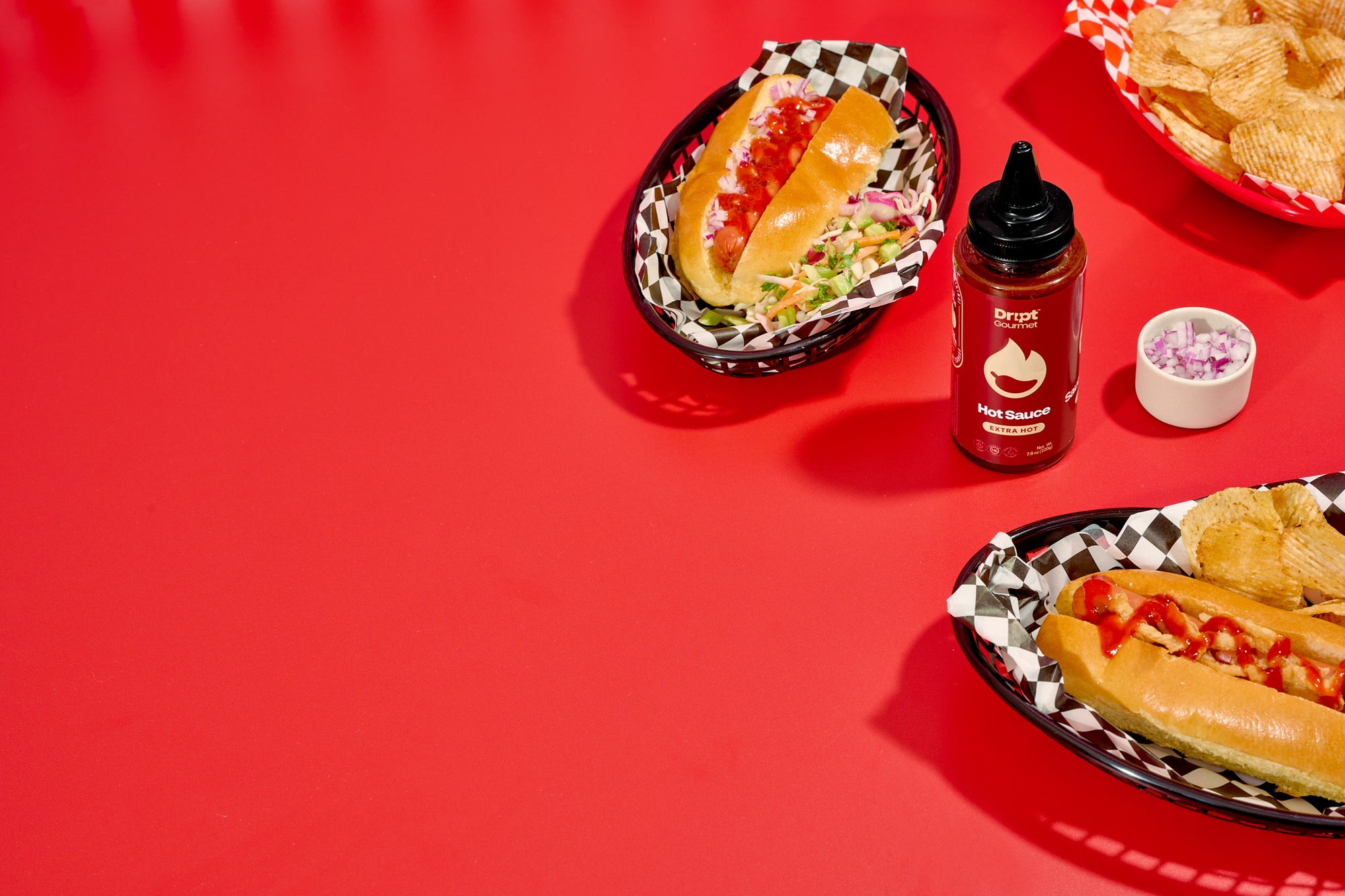 Dript Gourmet Extra Hot, Hot Sauce with classic hot dogs in baskets and on a red table. Artisanal Canadian hot sauce adding bold flavour to lunch.
