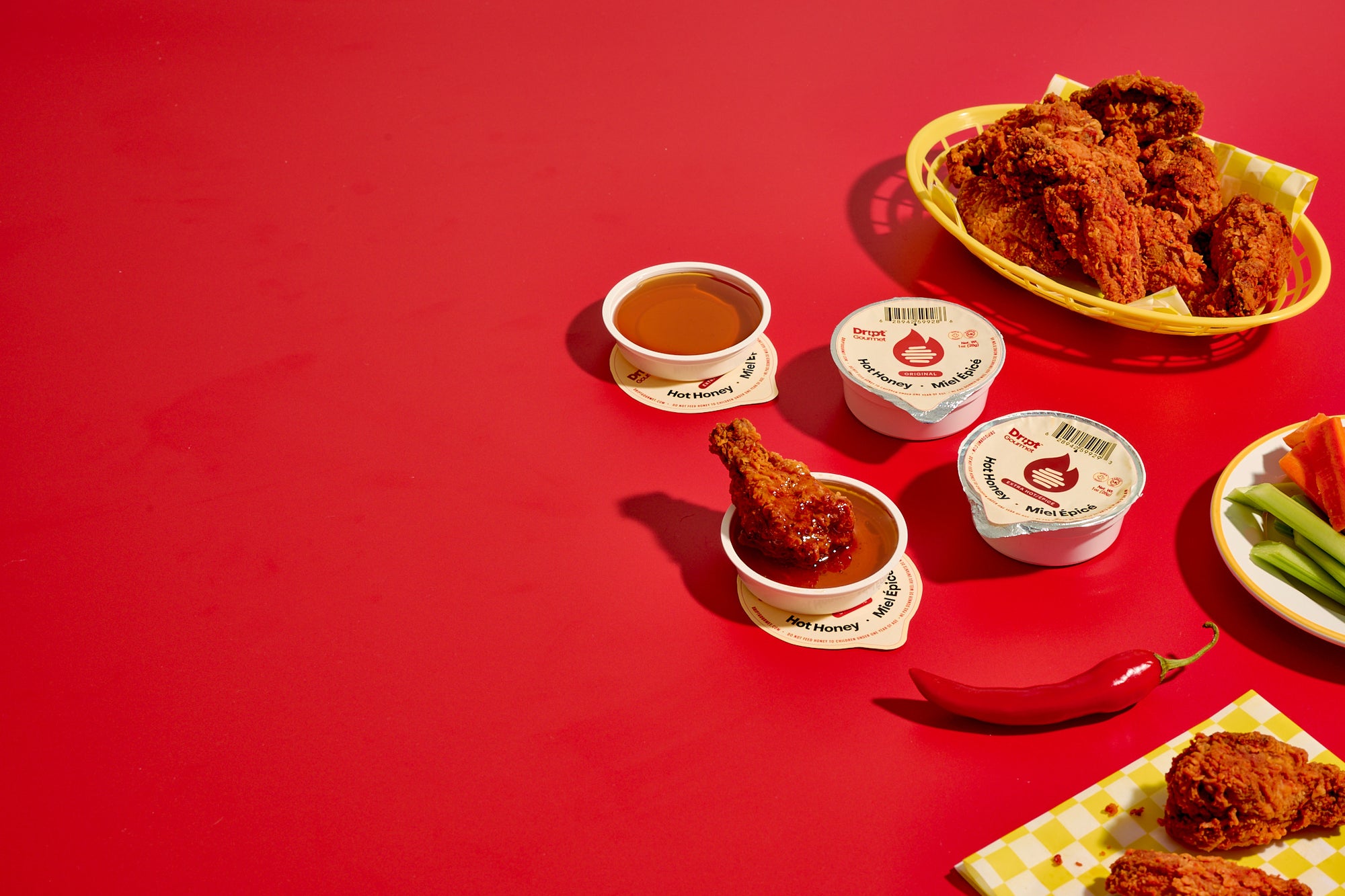 Dript Gourmet hot honey packs with breaded wings on a red table.