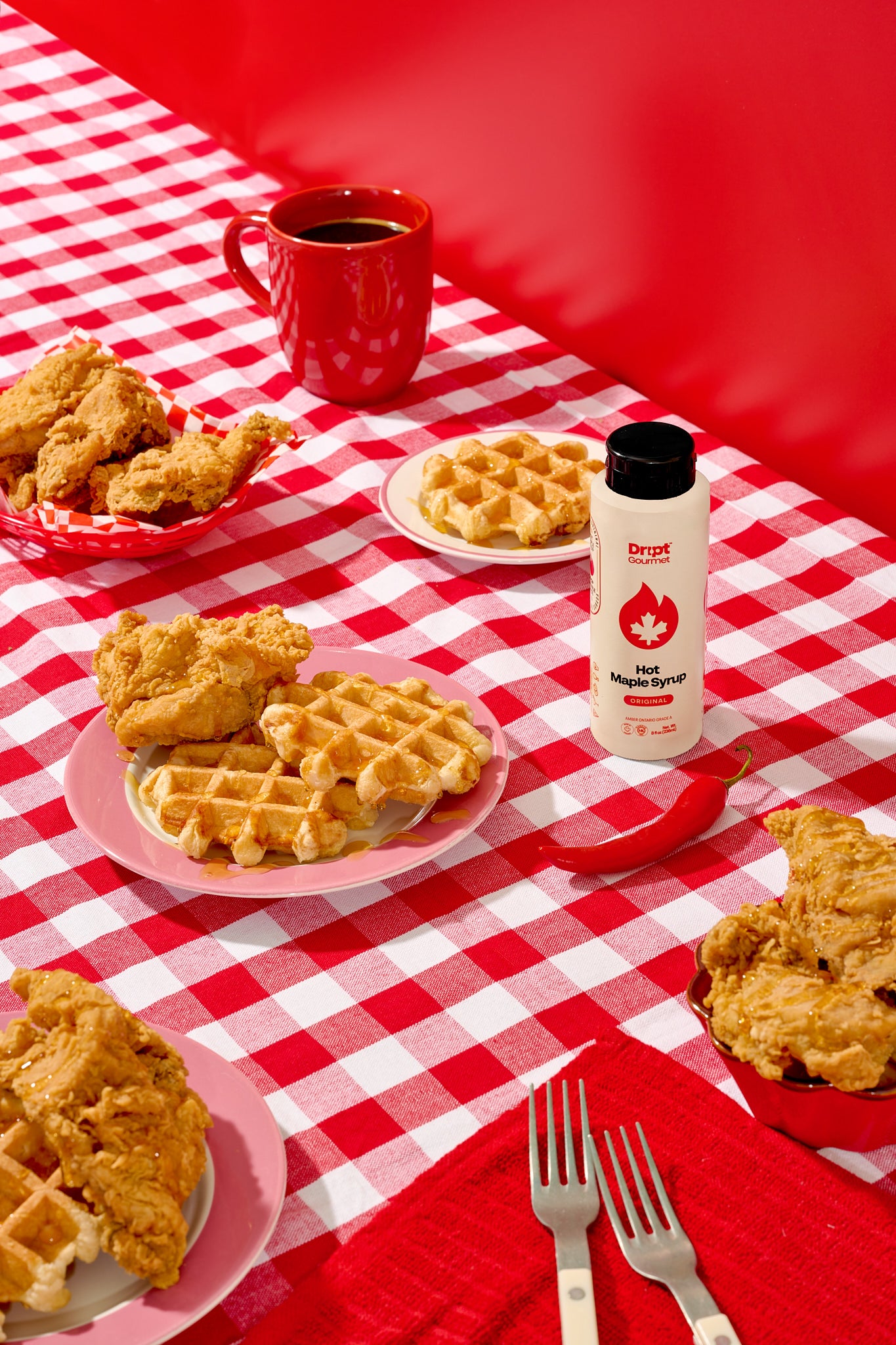Fried chicken and waffles on a red and white checkered tablecloth with a bottle of Dript Gourmet Original Hot Maple Syrup.