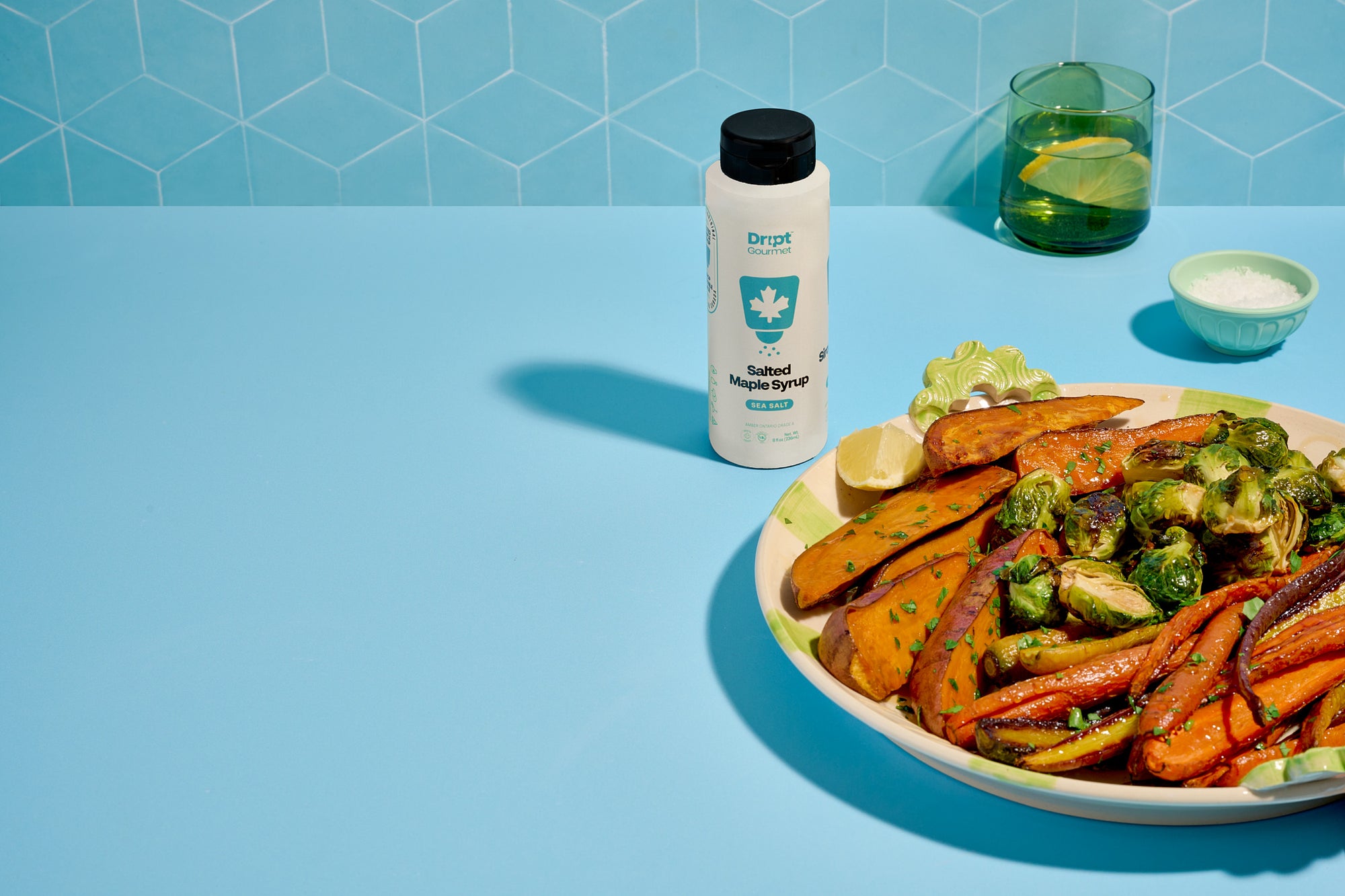 Dript Gourmet Salted Maple Syrup bottle with roasted veggies on a light blue table. Artisanal Canadian maple syrup infused with sea salt.