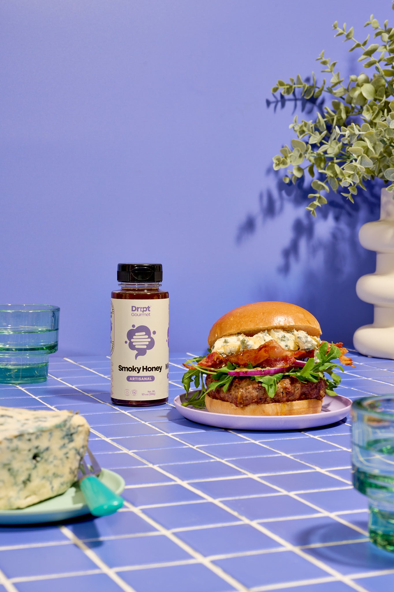 Dript Gourmet Smoky Honey with gourmet sandwich on a light blue tiled tables. Small-batch Canadian honey infused with smoky flavour.