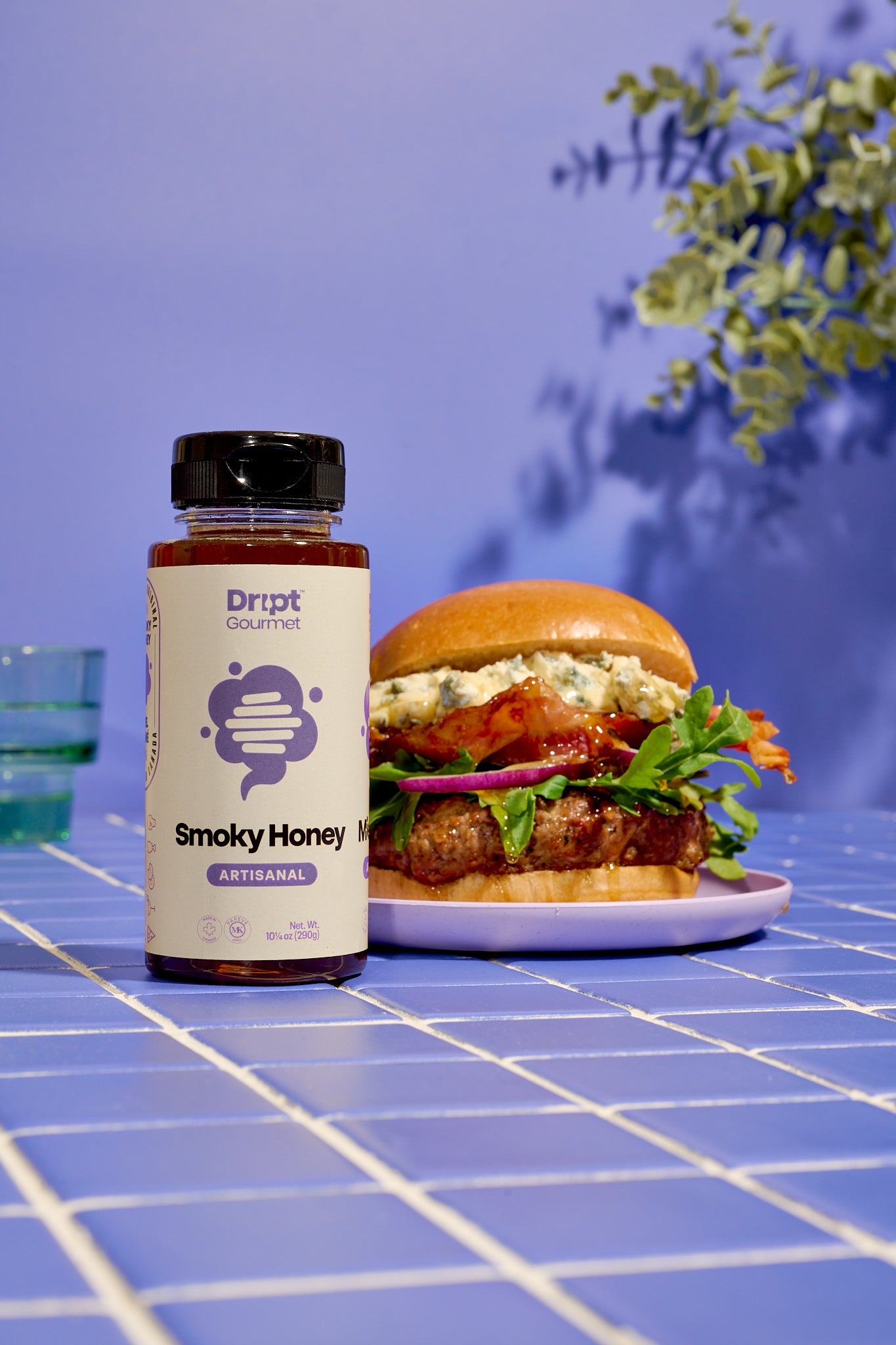 Dript Gourmet Smoky Honey with gourmet sandwich on a light blue tiled tables. Small-batch Canadian honey infused with smoky flavour.