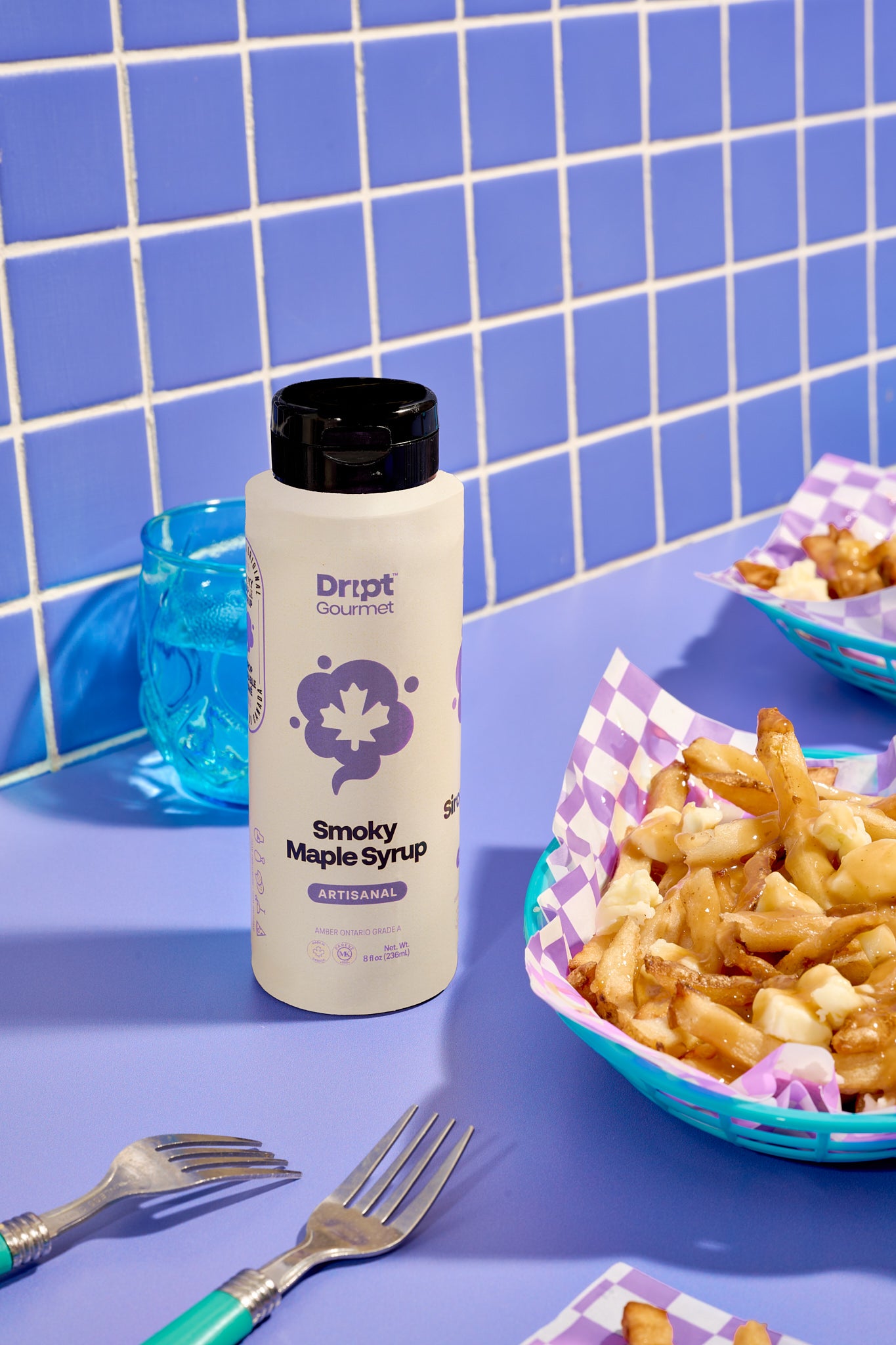 Dript Gourmet Smoky Maple Syrup bottle with poutine on a light purple table. Small-batch Canadian artisanal condiment with bold smoky flavour.