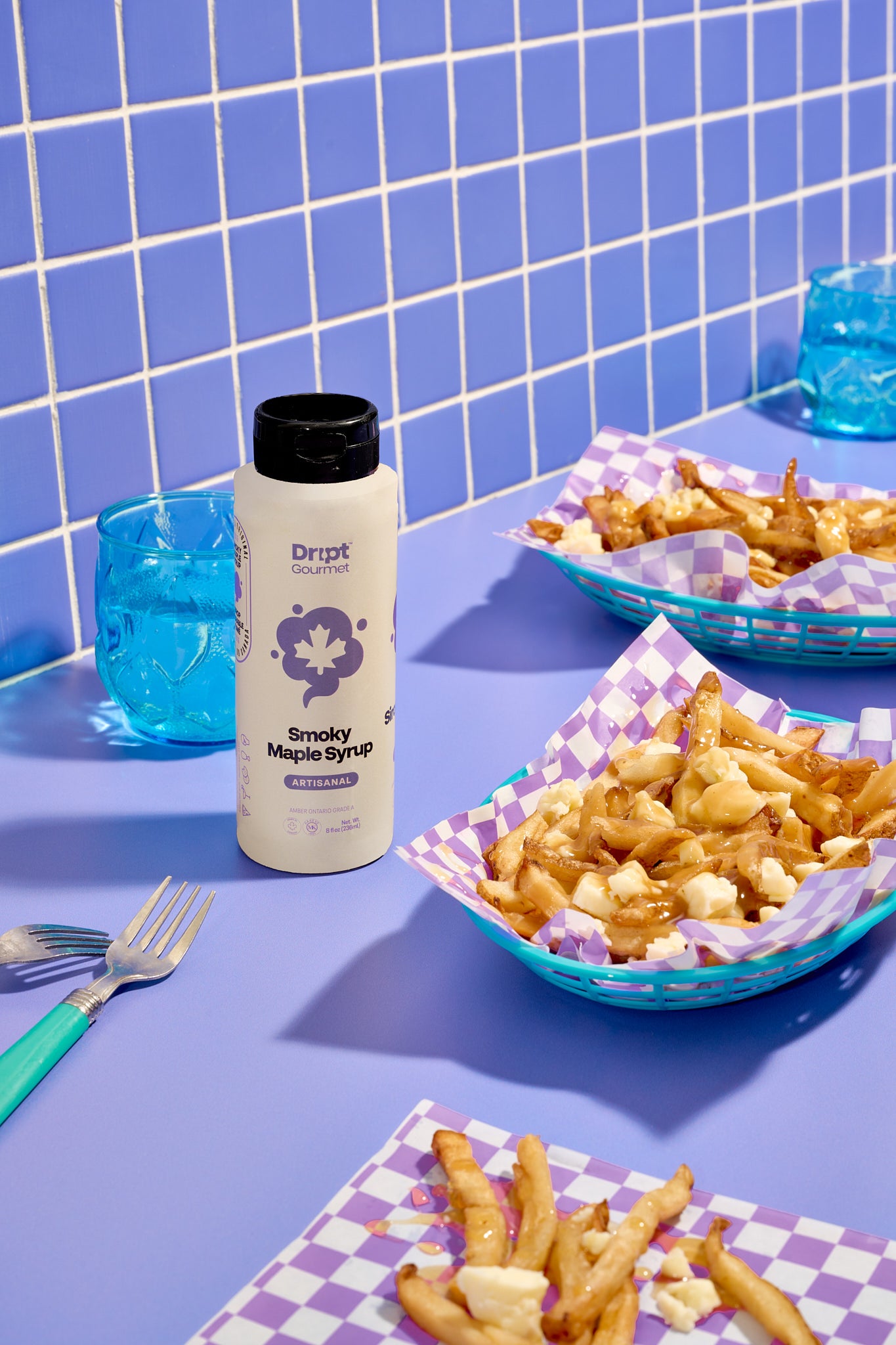 Dript Gourmet Smoky Maple Syrup bottle with poutine on a light purple table. Small-batch Canadian artisanal condiment with bold smoky flavour.